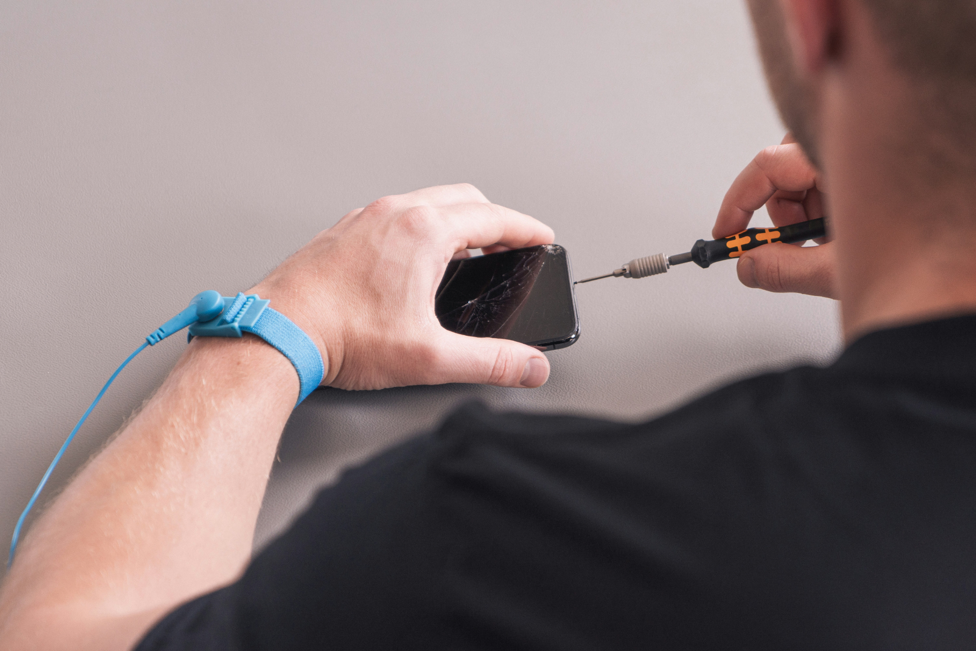 Technician removing screws from a cracked phone screen at the repair bench